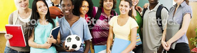 Teenage students standing in front of the blackboard with their teacher and looking at the camera.